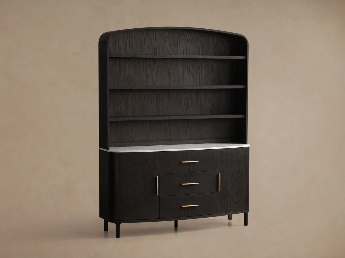 Front view of the black oak Danny Hutch with Drawers, featuring a white Carrara marble top, three brass-handled drawers, and two curved doors. Three open shelves are above.