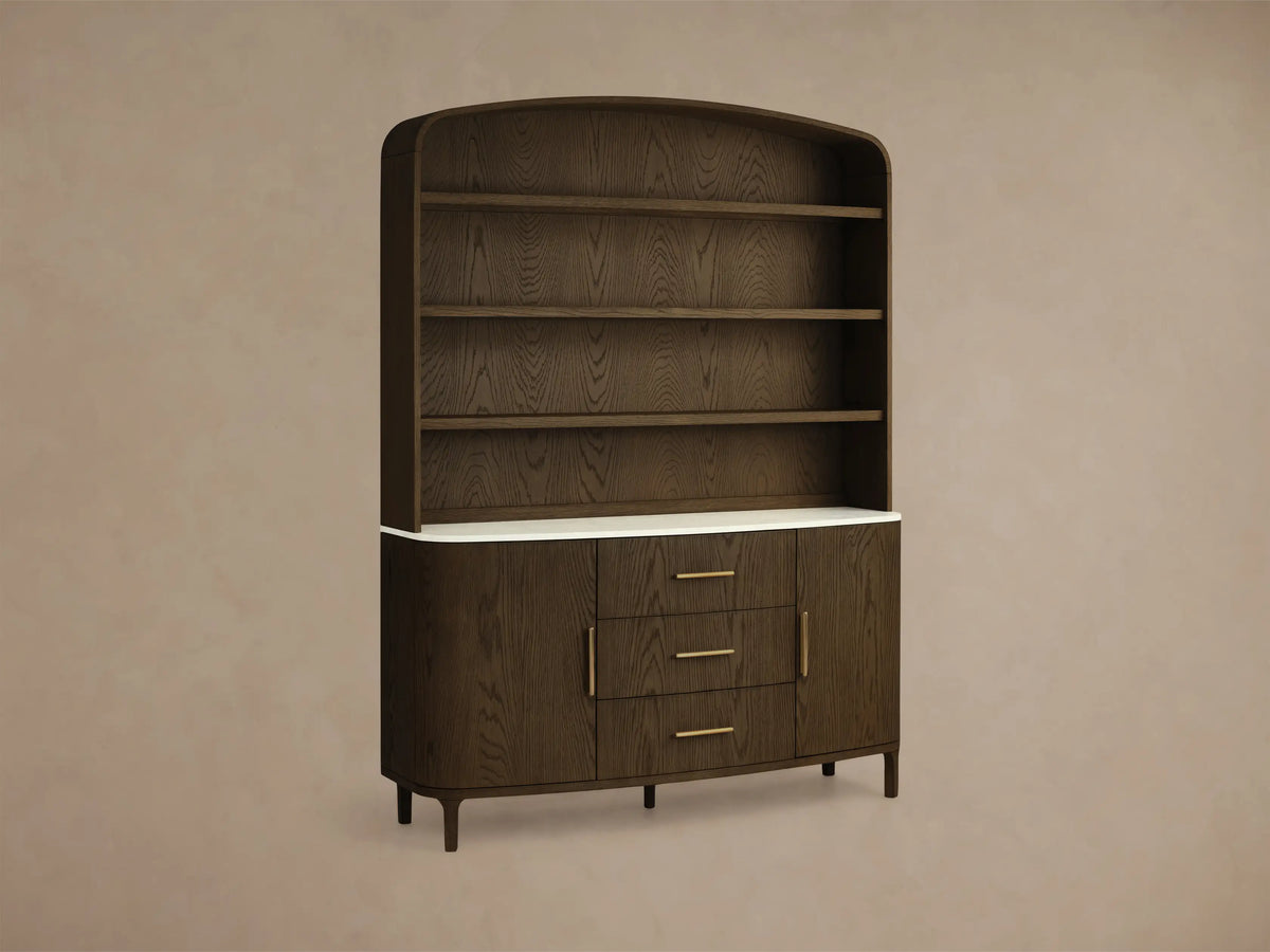 Front view of the dark oak Danny Hutch with Drawers, with an arched top, three open shelves, white marble, three drawers, and brass pulls.