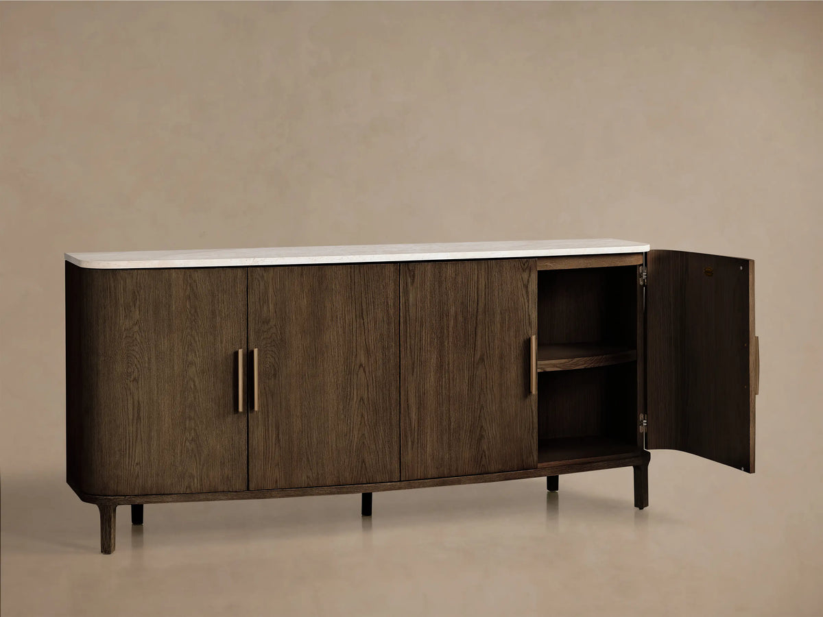 Front view of a dark brown wooden sideboard with a white marble top, curved ends, and four doors featuring gold bar handles.