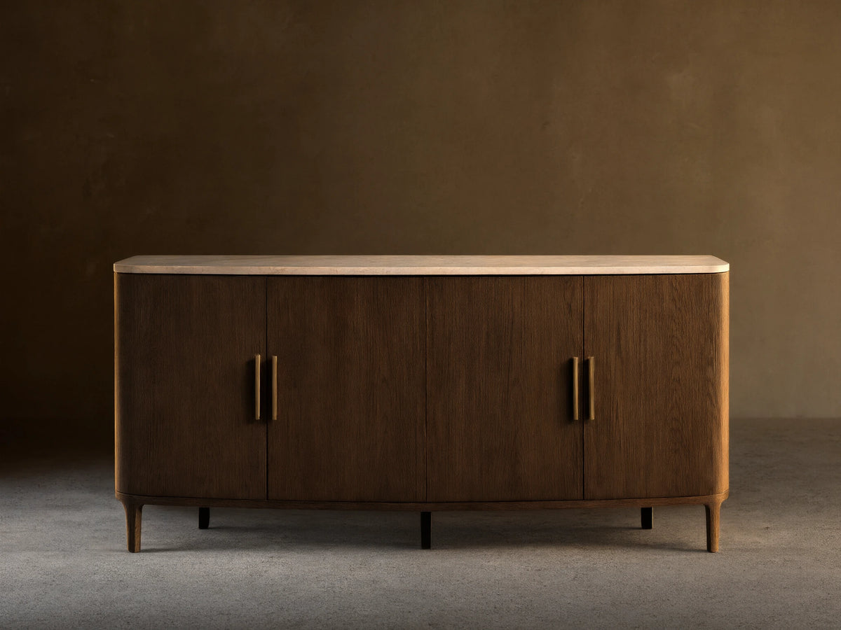 Front view of a dark brown wooden sideboard with a white marble top, curved ends, and four doors featuring gold bar handles.