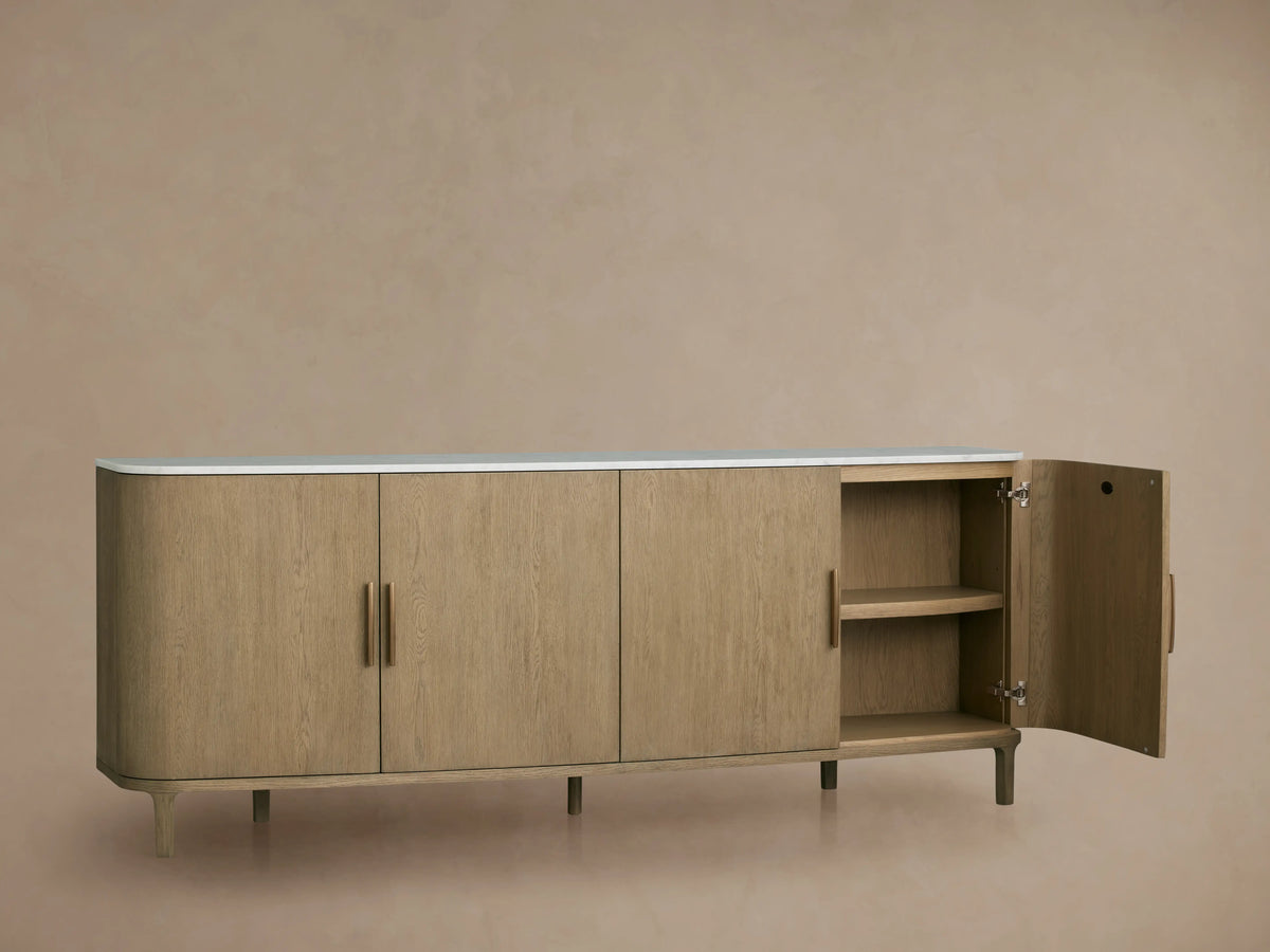 Danny Sideboard with oak wood finish and white marble top. Features open door showing shelves, brass handles, and slender legs.