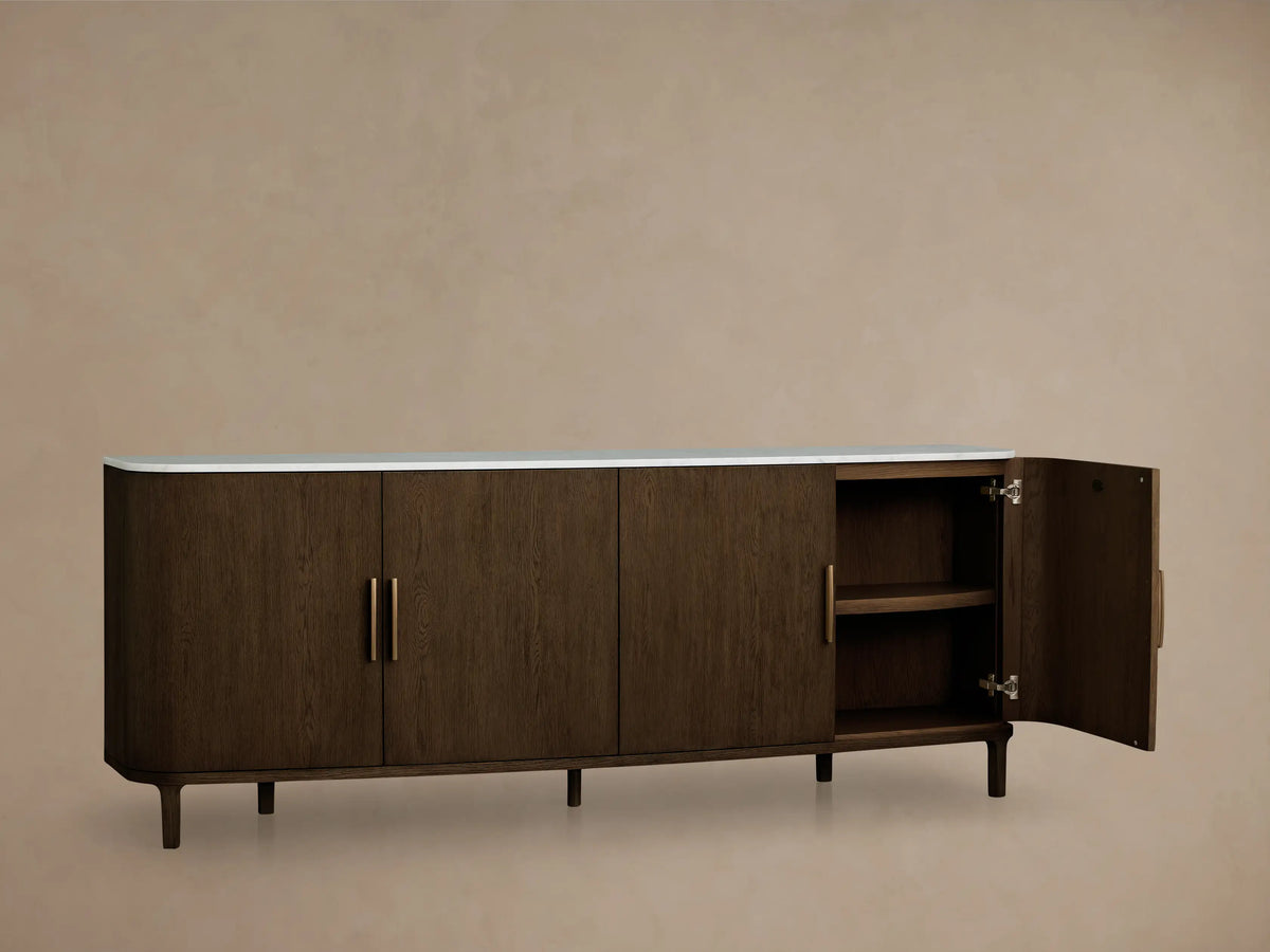 Front view of a dark brown wooden cabinet with curved ends, a white top, four doors, and vertical gold handles.