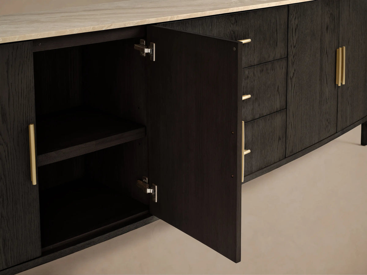 Front view of dark oak Danny Sideboard with Drawers. Features a cream marble top, three center drawers with brass pulls, and cabinet doors. Left door open to a shelf.