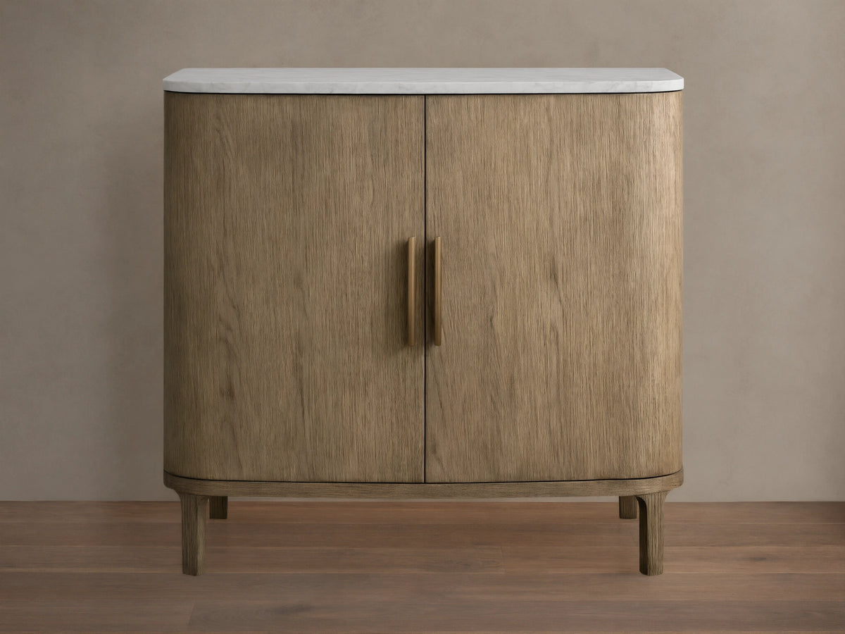 Oak Danny Cabinet with a hand-applied finish, features a smooth white Carrara marble top. Two doors with central handles, resting on short legs.