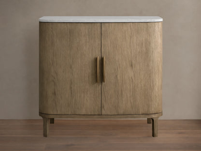 Oak Danny Cabinet with a hand-applied finish, features a smooth white Carrara marble top. Two doors with central handles, resting on short legs.