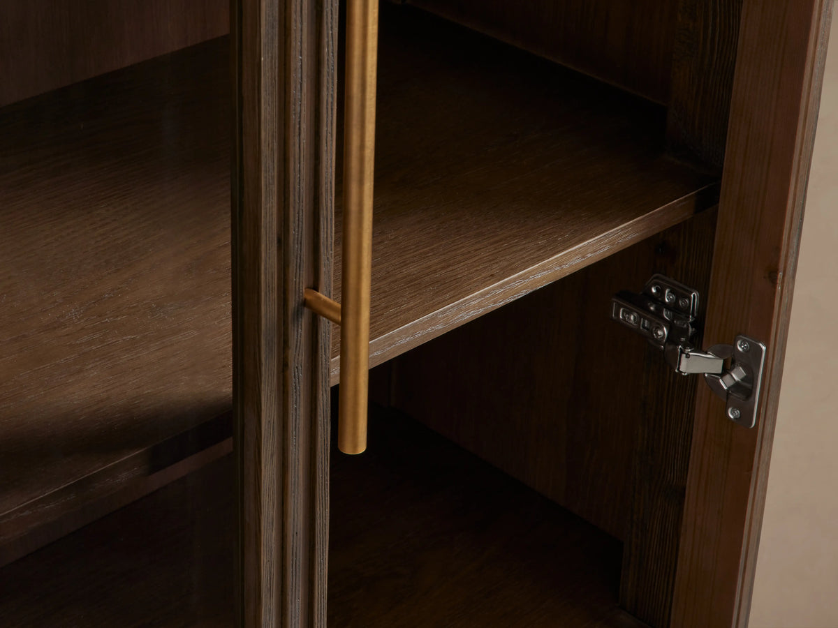Finnley Glass Cabinet with dark wood finish, two glass doors with brass pulls, four visible shelves, and a brass base.