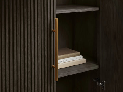 Ebony Finnley Cabinet with vertically fluted doors, brass pulls, and a golden plinth base against a neutral wall.