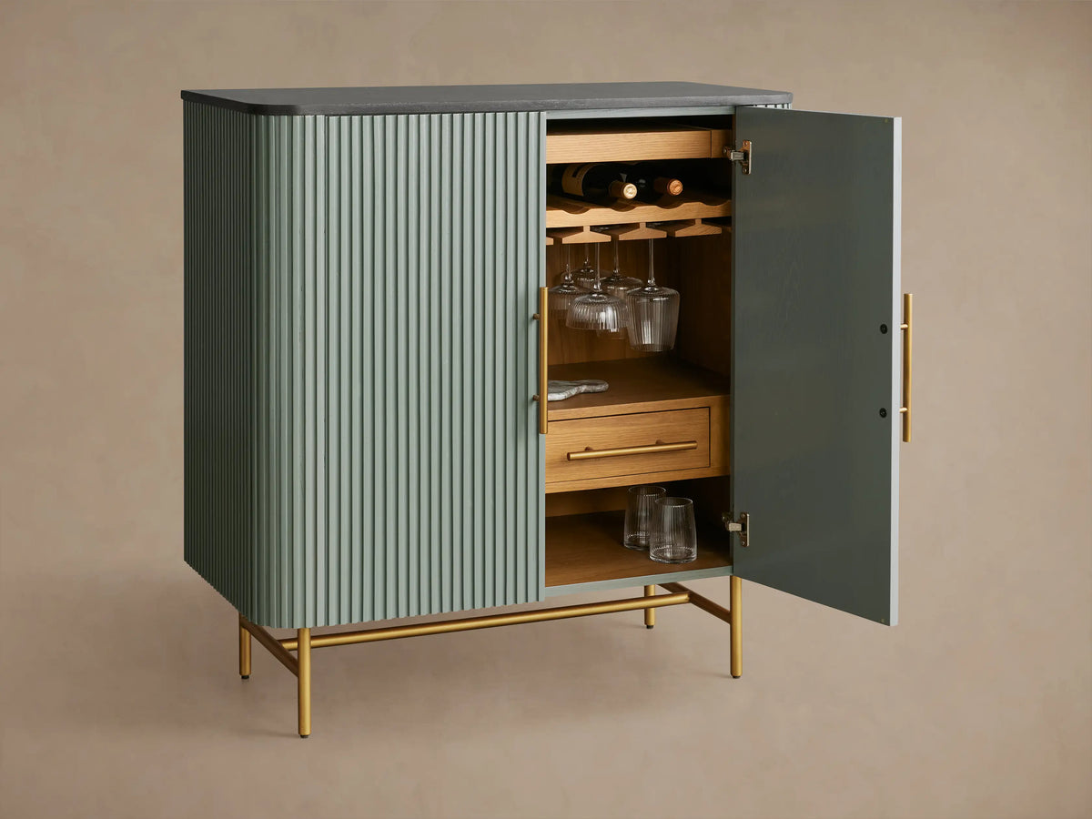 Finnley Bar Cabinet in pumice with vertical reeding detail, dark top, and gold brass-finished handles & legs.