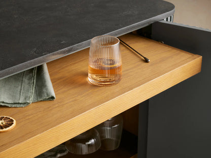 Finnley Bar Cabinet, sage green reeded exterior, dark grey top, gold legs. Right door open, showing wine bottles, glasses, drawer.