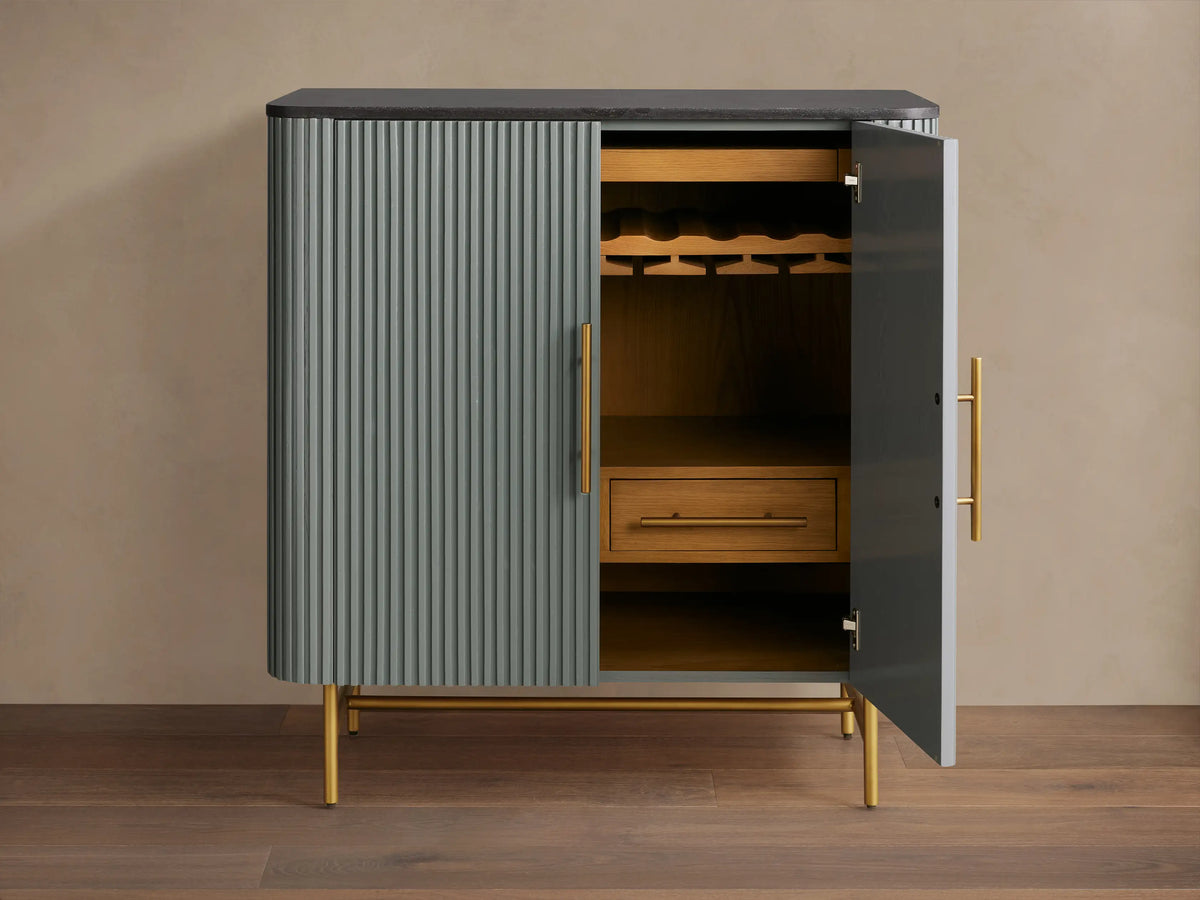 Finnley Bar Cabinet, close-up interior. Oak wood, hanging ribbed wine glasses, white marble surface, two drawers with brass pulls.