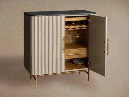Finnley Bar Cabinet with dark top, reeded light-colored doors, vertical brass handles, and thin brass legs on wood floor.