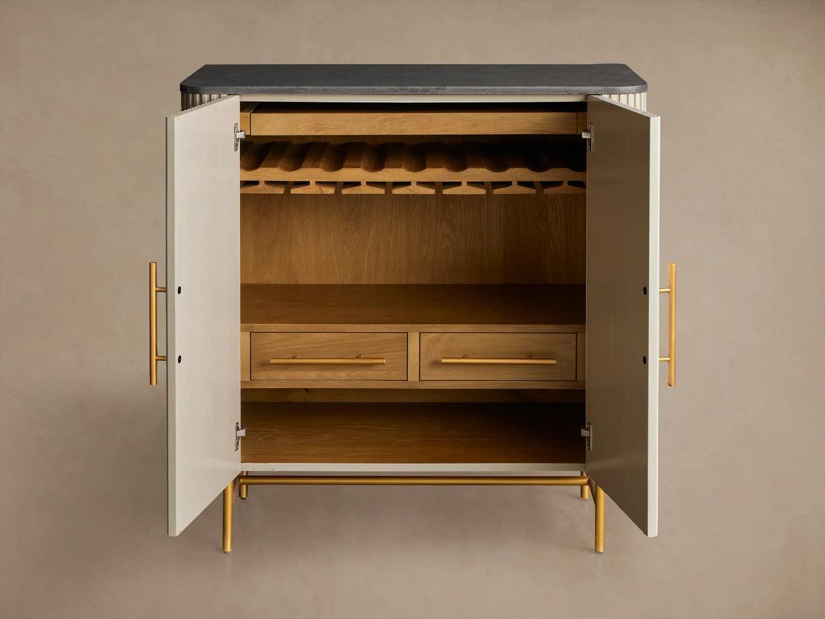 Close-up of open Finnley Bar Cabinet, light beige ribbed door, brass pull, oak interior with wine bottles, 2 hanging glasses.