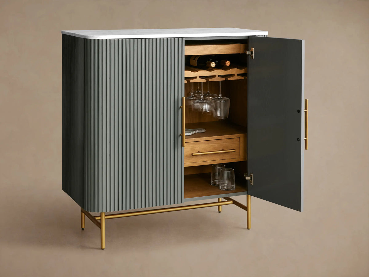 Finnley Bar Cabinet with gray-green ribbed facade, white marble top, and brass legs. Right door open, revealing wood wine storage.