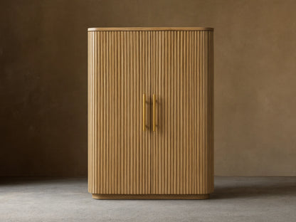 Finnley Wood Bar Cabinet with a honey finish, featuring vertical ribbed design, two central gold handles, and curved edges.