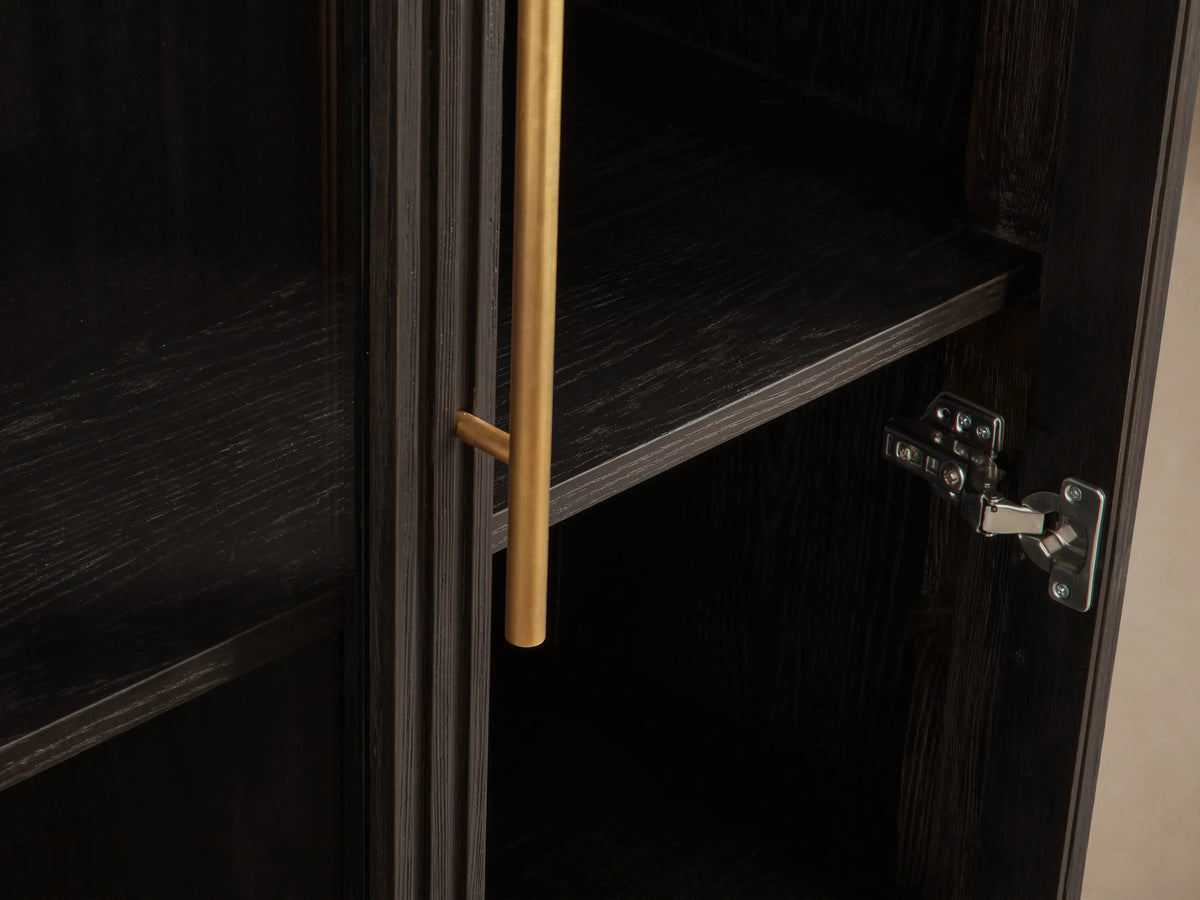 Finnley Glass Cabinet, dark ebony wood with fluted sides, two glass doors with brass pulls, and a brass plinth base.