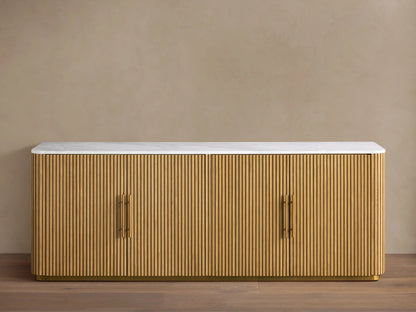 Finnley Plinth Sideboard with honey finish, ribbed white oak wood design, brass hardware, and white marble top against a neutral background.