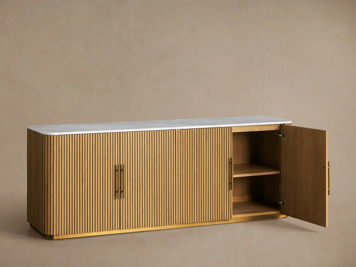 Finnley Plinth Sideboard with honey finish, ribbed white oak wood design, brass hardware, and white marble top against a neutral background.