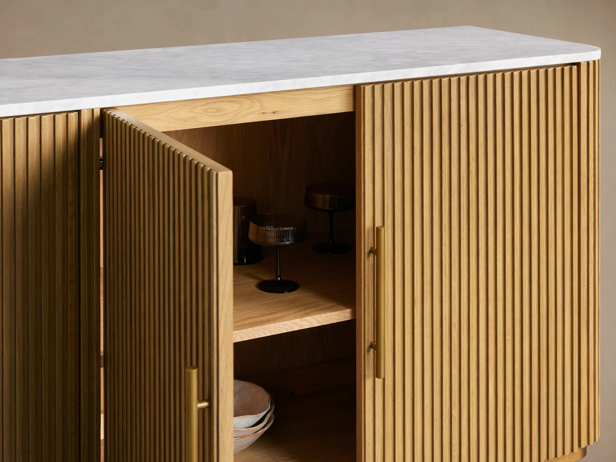 Finnley Plinth Sideboard in honey finish with vertical grooves, open door revealing shelves, white stone top, brass handles.