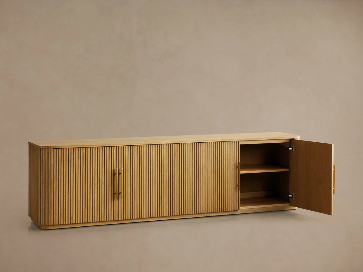 Finnley Wood Media Console with a ribbed front design in Honey finish, featuring brass-finished handles, set against a neutral wall.