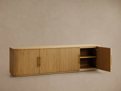 Finnley Wood Media Console with a ribbed front design in Honey finish, featuring brass-finished handles, set against a neutral wall.