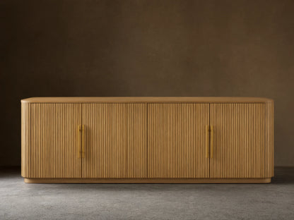 Finnley Wood Media Console with a ribbed front design in Honey finish, featuring brass-finished handles, set against a neutral wall.