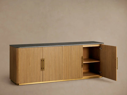 Finnley Plinth Sideboard with ribbed honey finish, black top, brass handles, and plinth base, against a neutral wall.