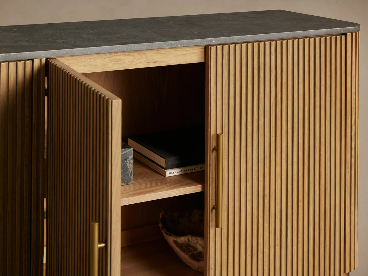 Finnley Plinth Sideboard with a honey finish, two cabinet doors, one open, showing shelves, and a dark stone top.