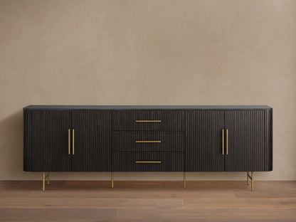Finnley Sideboard with three central drawers and two cabinet doors, black finish, brass handles, and slender legs, against a beige wall.