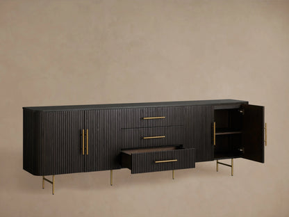 Finnley Sideboard with three central drawers and two cabinet doors, black finish, brass handles, and slender legs, against a beige wall.