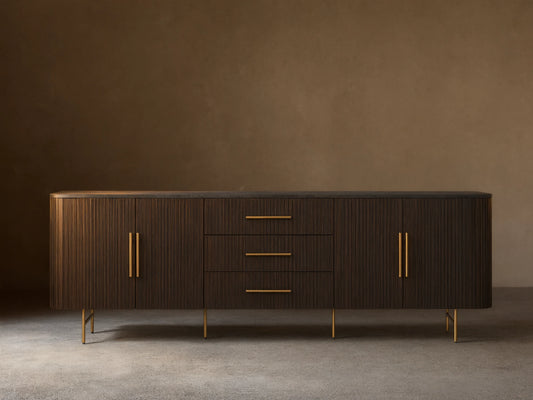 Finnley Sideboard with three central drawers and two cabinet doors, black finish, brass handles, and slender legs, against a beige wall.