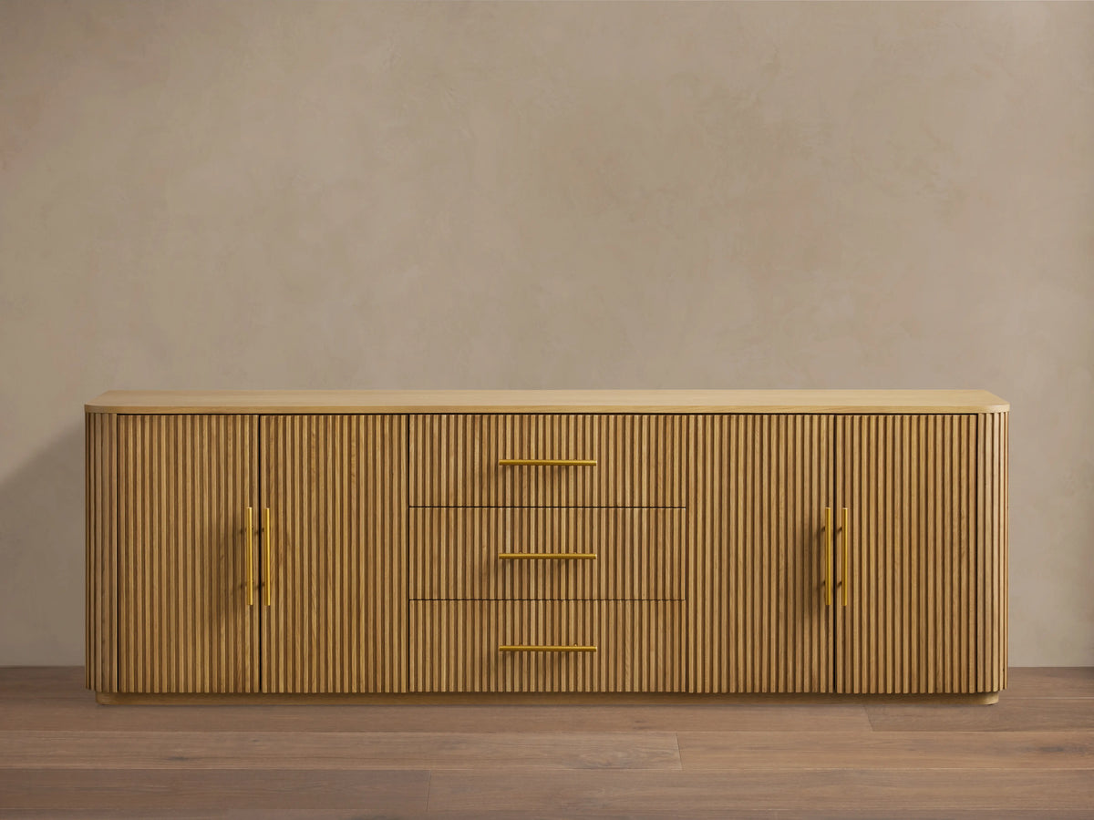 Finnley Wood Sideboard with a honey finish, featuring three central drawers and fluted design doors on each side, with brass-finished handles.