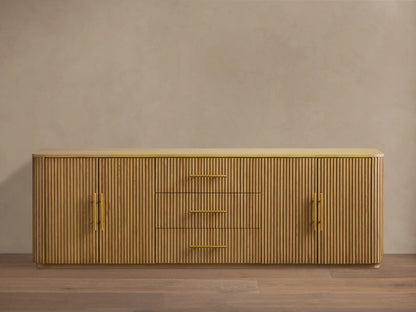 Finnley Wood Sideboard with a honey finish, featuring three central drawers and fluted design doors on each side, with brass-finished handles.