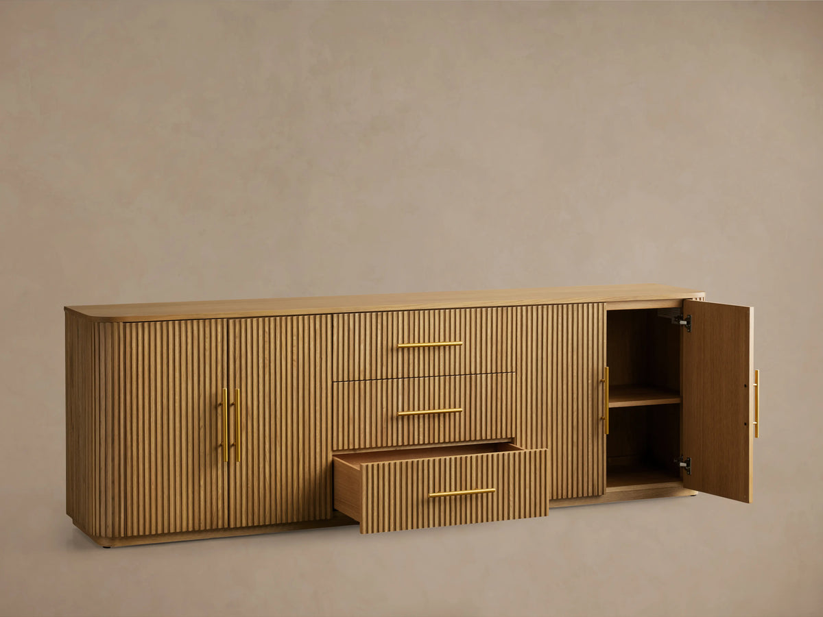 Finnley Wood Sideboard with a honey finish, featuring three central drawers and fluted design doors on each side, with brass-finished handles.