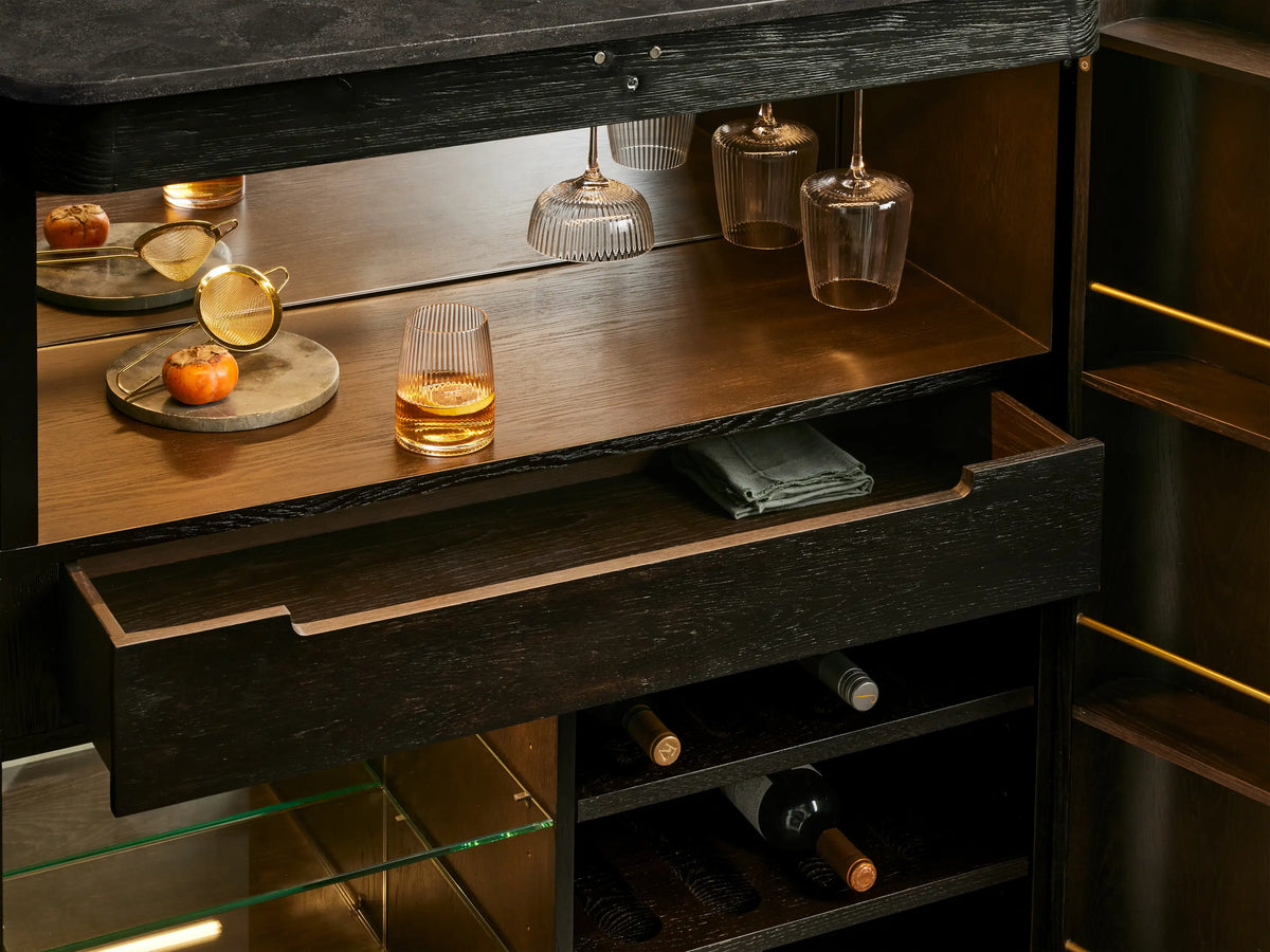 Open Finnley Plinth Bar Cabinet, dark wood, brass plinth and hardware. Filled with wine bottles, glasses, bar tools, mirrors.