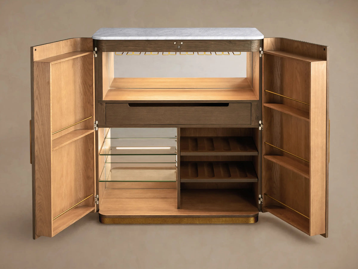Finnley Plinth Bar Cabinet, dark fluted wood, white marble top, brass base. Open, revealing wine, glasses, bar tools.