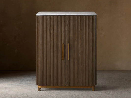 Finnley Plinth Bar Cabinet with dark fluted wood doors, white marble top, brass handles, and plinth base.
