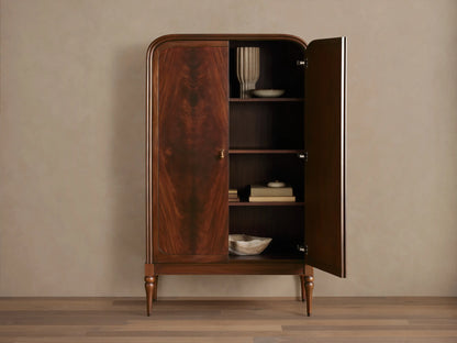 Frances Cabinet: Dark mahogany cabinet with book-matched figured veneer, rounded top, brass handles, turned legs, on a wood floor.