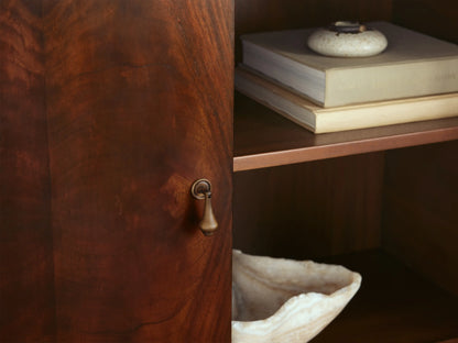 Frances Cabinet, dark mahogany with book-matched figured veneer, rounded top, two doors with brass knobs, tapered legs.