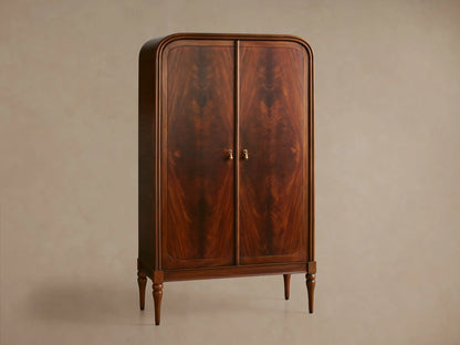 Close-up of Frances Cabinet's dark mahogany door with figured grain, brass handle, and interior shelves with books and bowl.