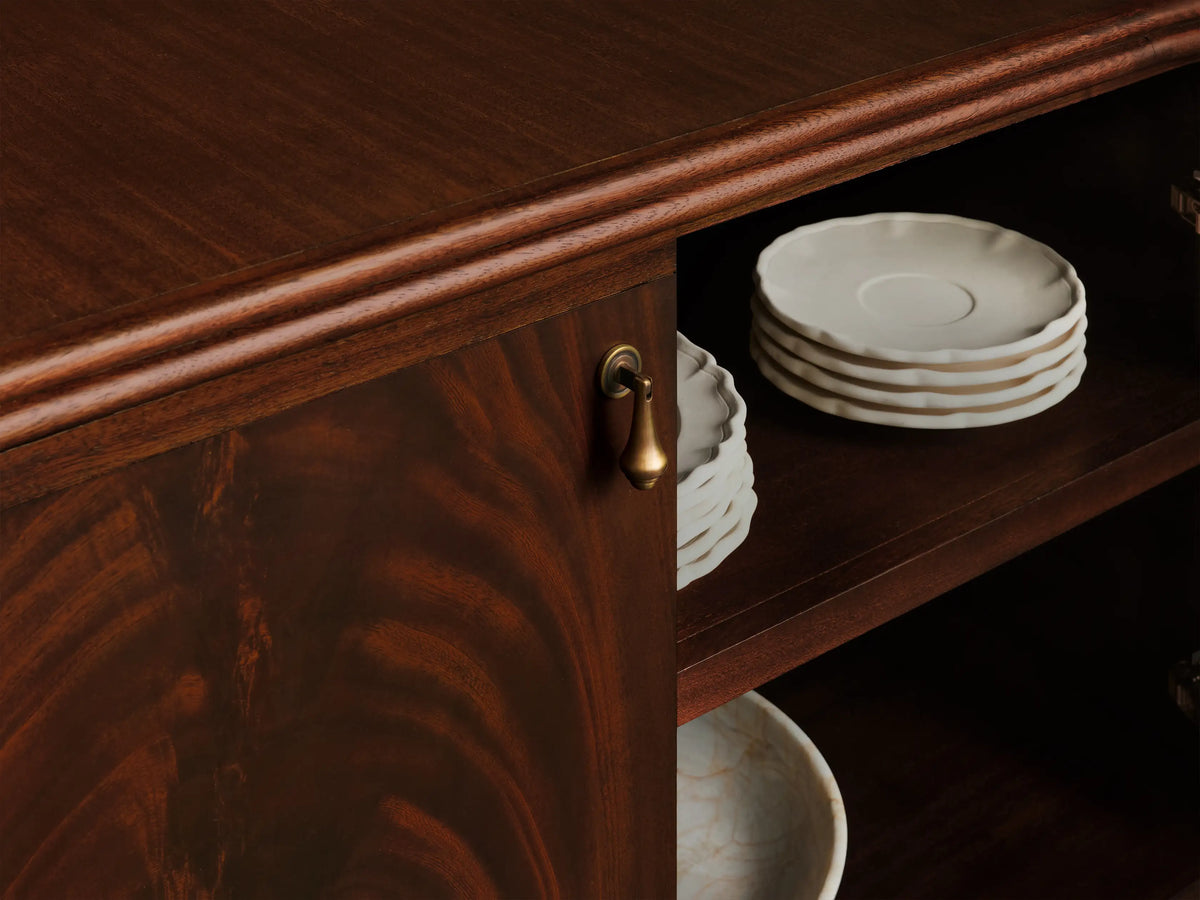 Frances Sideboard, dark mahogany with flame grain. Rounded left, closed doors with brass pulls. Right doors open, showing shelves. Tapered legs.