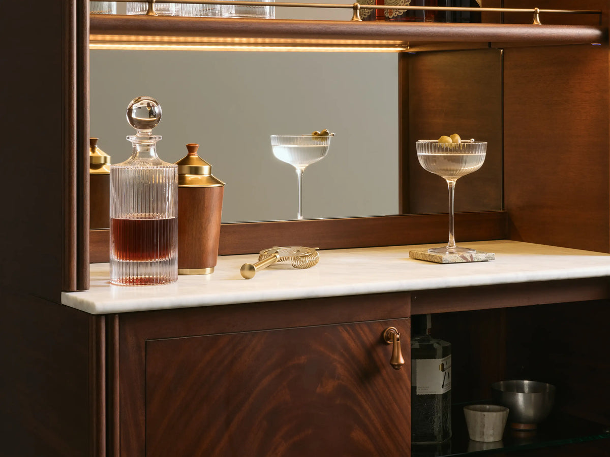 Interior view of the dark mahogany Frances Bar Cabinet, with illuminated mirror, white marble top, decanter, shaker, and brass hardware.