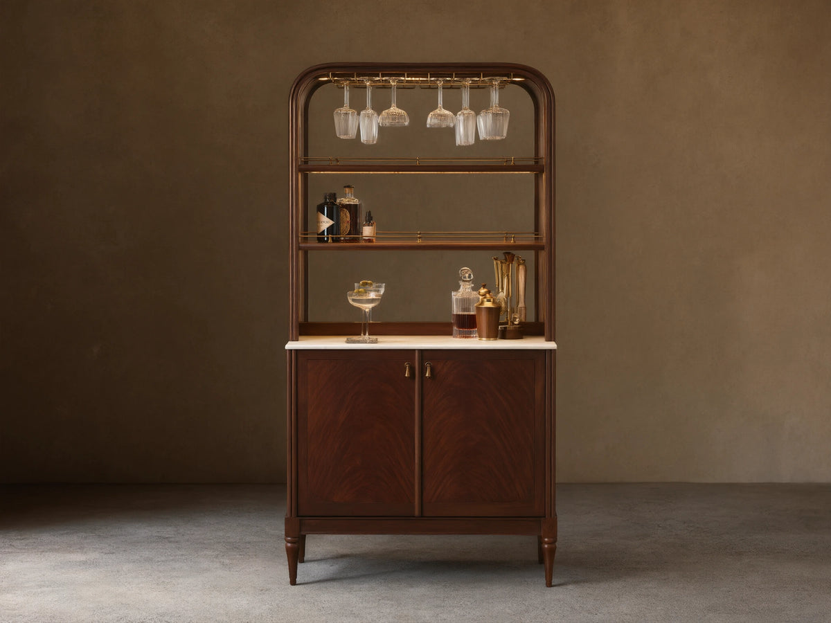 Front view of the Frances Bar Cabinet in dark mahogany with flame grain, brass stemware rack, marble top, and spirits.