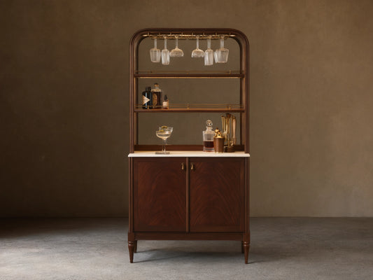 Front view of the Frances Bar Cabinet in dark mahogany with flame grain, brass stemware rack, marble top, and spirits.