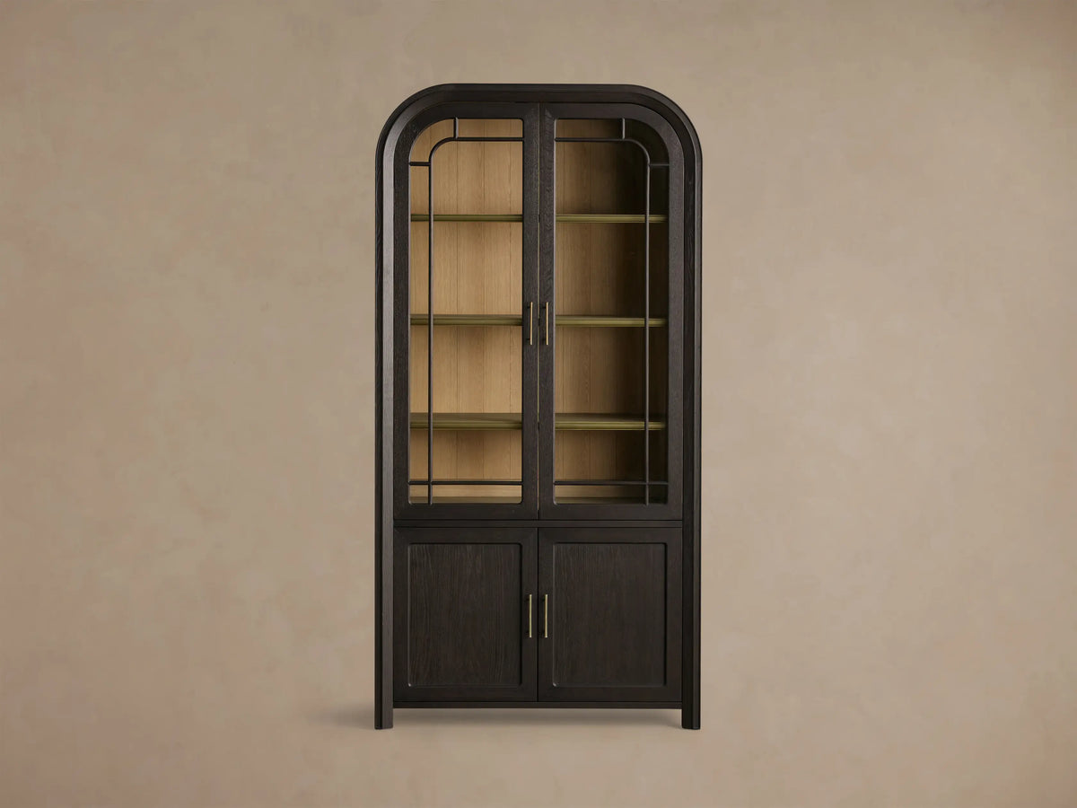 Close-up of dark mocha-toned Gatlin Glass Cabinet's glass door, showing light wood shelves, brass rail, and decorative items.