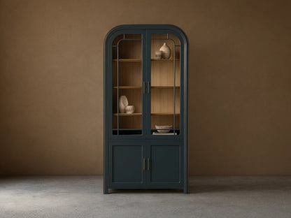 Front view of the Dark Blue Gatlin Glass Cabinet with an arched top, glass doors, wood shelves, and brass pulls.