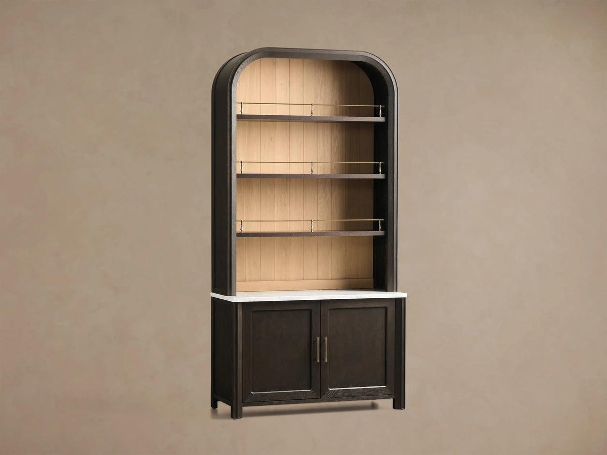 Front view of dark brown Gatlin Hutch with arched open shelves, light wood back, brass rails, white marble top, and two-door cabinet.