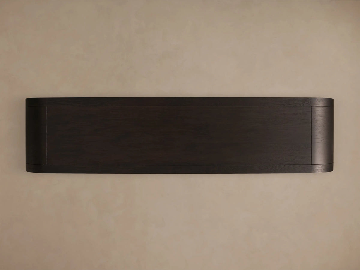 Close-up of the dark wood Gatlin Sideboard, featuring a rounded corner, glass door with a brass pull, and light wood interior shelves.