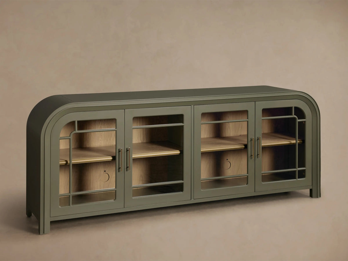 Front view of a green Gatlin Sideboard with four tempered glass doors, rounded ends, and antique brass pulls, displaying items on wood shelves.