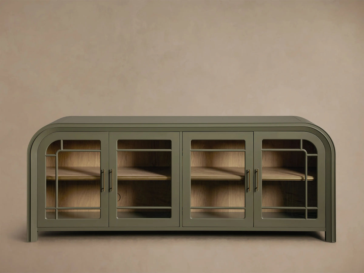 Close-up of the Olive Green Gatlin Sideboard with rounded corners, open glass door revealing wooden shelves, dark glasses, and brass pull.