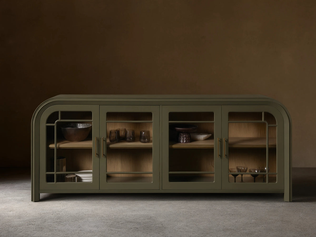 Front view of a green Gatlin Sideboard with four tempered glass doors, rounded ends, and antique brass pulls, displaying items on wood shelves.